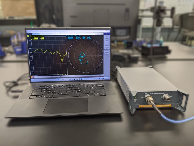 A Laptop running Bird TVNA software displaying 2 graphs connected to a BNA100 sitting on a desk with a lab in the background.